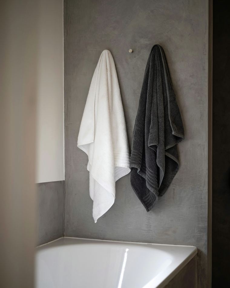 White and charcoal towels hanging on a concrete bathroom wall